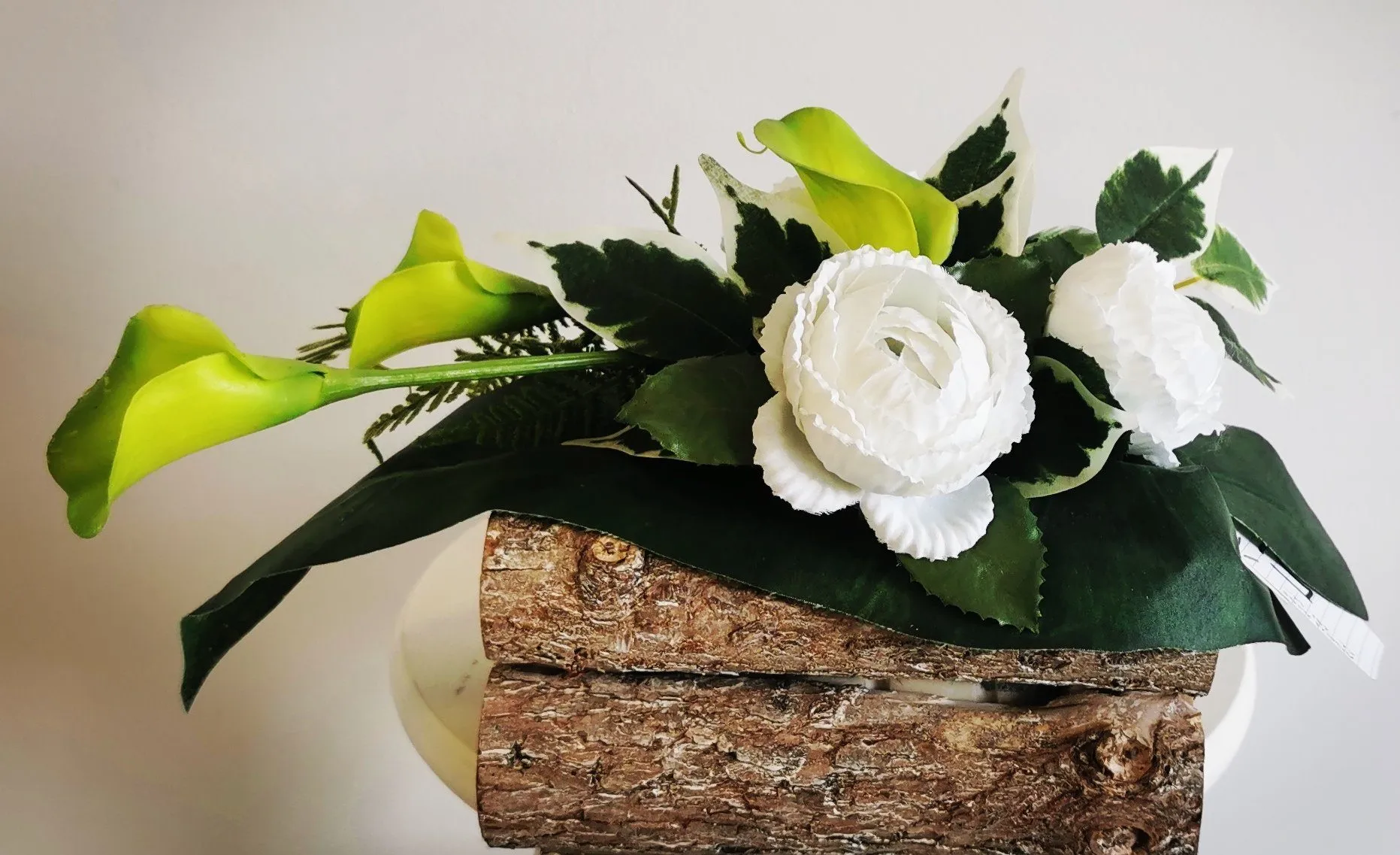 Arrangement floral de deuil composé de roses blanches et d'arums vert clair sur bûche