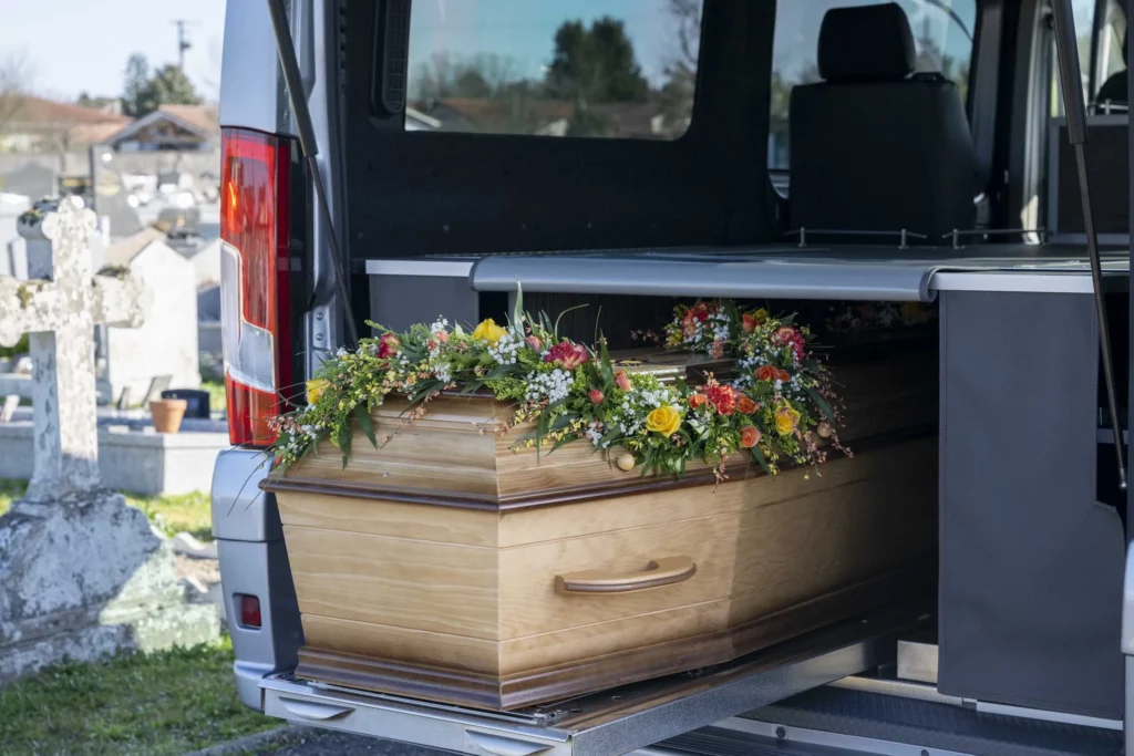 Cercueil en bois sous composition florale dans un véhicule funéraire